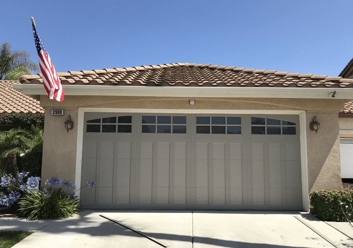 Tan carriage-style garage door with window lites on a tile-roof home